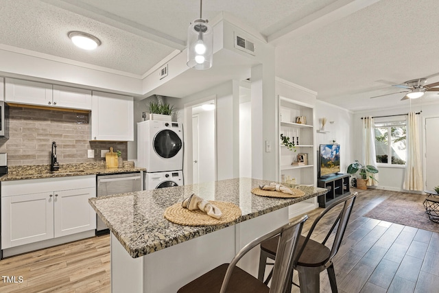 7002 Longstreet Dr Unit C, Raleigh, NC 27615 - kitchen with estacked washer and dryer, a textured ceiling, stainless steel dishwasher, light wood finished floors, and light stone counters
