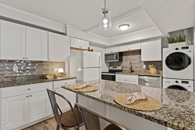 7002 Longstreet Dr Unit C, Raleigh, NC 27615 - kitchen featuring appliances with stainless steel finishes, stacked washer / drying machine, a textured ceiling, a breakfast bar, and white cabinetry