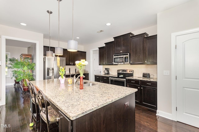 1726 Rapids Ct, Franklinton, NC 27525 - kitchen with appliances with stainless steel finishes, light stone counters, dark brown cabinetry, a kitchen island with sink, and decorative light fixtures