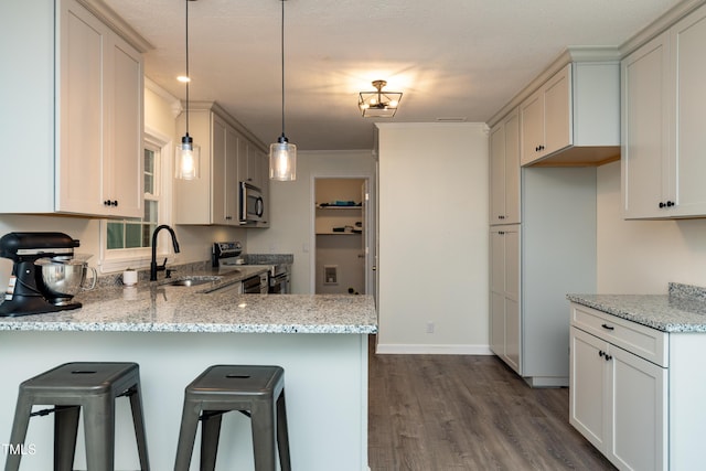438 N Hickory St, Angier, NC 27501 - kitchen with appliances with stainless steel finishes, a peninsula, dark wood-style flooring, light stone countertops, and a kitchen bar