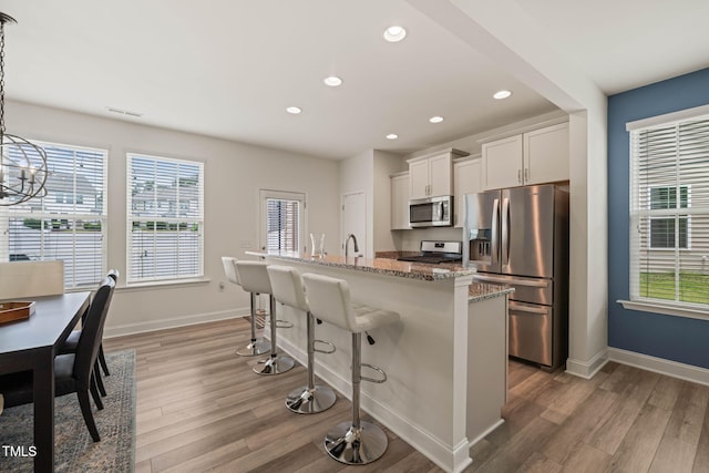 1137 Amber Shadow Dr, Durham, NC 27703 - kitchen with appliances with stainless steel finishes, light wood finished floors, a kitchen bar, recessed lighting, and an island with sink