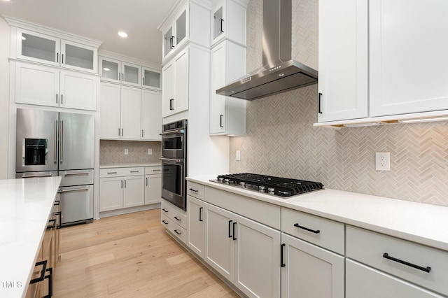 1417 Westmoreland Dr, Raleigh, NC 27612 - kitchen featuring wall chimney exhaust hood, stainless steel appliances, decorative backsplash, white cabinetry, and light wood-type flooring