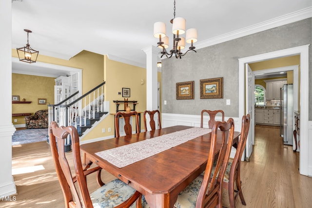 9009 Hometown Dr, Raleigh, NC 27615 - dining room featuring light wood-style floors, a chandelier, ornamental molding, ornate columns, and stairs