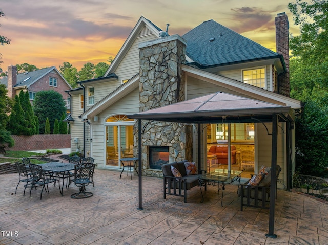 9009 Hometown Dr, Raleigh, NC 27615 - back of property at dusk with a chimney, a patio area, roof with shingles, and stone siding