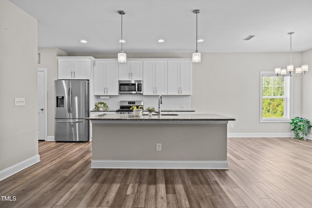40 Cinnamon Teal Way, Youngsville, NC 27596 - kitchen with stainless steel appliances, wood finished floors, a kitchen island with sink, backsplash, and dark stone countertops