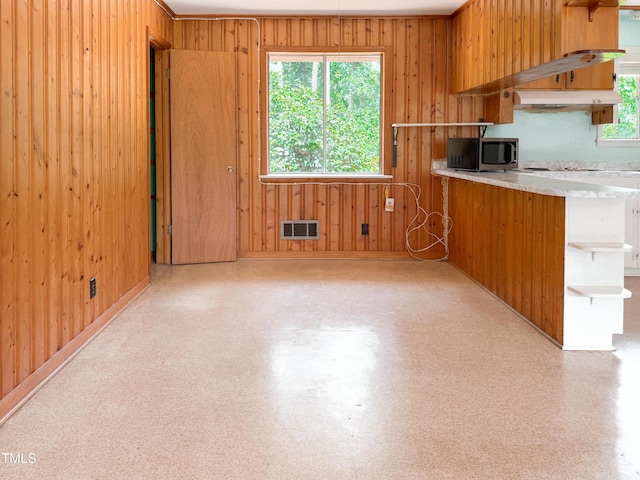 3323 Baugh St, Raleigh, NC 27604 - kitchen featuring stainless steel microwave, open shelves, wood walls, under cabinet range hood, and brown cabinets