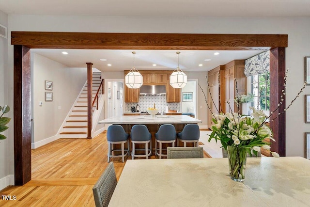 1054 Canterbury Ln, Chapel Hill, NC 27517 - kitchen featuring wall chimney exhaust hood, decorative backsplash, light countertops, light wood finished floors, and a kitchen breakfast bar
