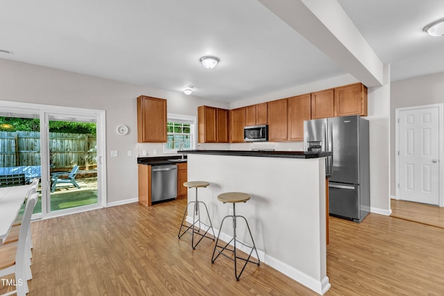 3119 Guiding Light Rd, Raleigh, NC 27610 - kitchen featuring appliances with stainless steel finishes, light wood-style flooring, dark countertops, and a kitchen bar