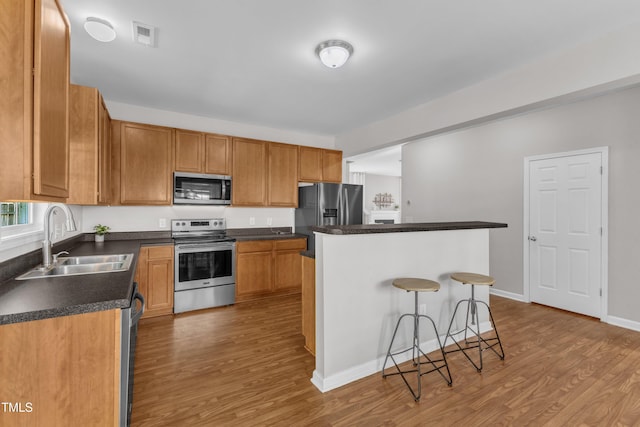 3119 Guiding Light Rd, Raleigh, NC 27610 - kitchen with appliances with stainless steel finishes, wood finished floors, a kitchen bar, a center island, and dark countertops