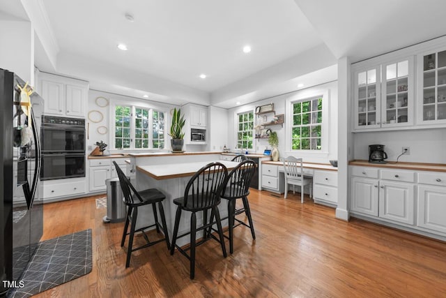 2602 Vintage Hill Ct, Durham, NC 27712 - kitchen with black appliances, white cabinets, a kitchen breakfast bar, light wood-type flooring, and built in study area