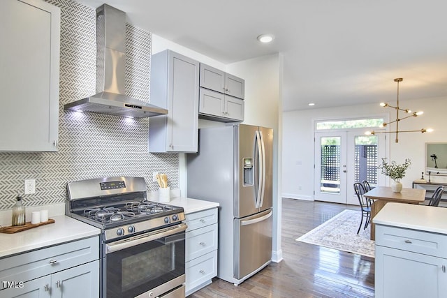 931 Ramseur St, Durham, NC 27701 - kitchen featuring stainless steel appliances, wall chimney range hood, gray cabinetry, wood finished floors, and backsplash