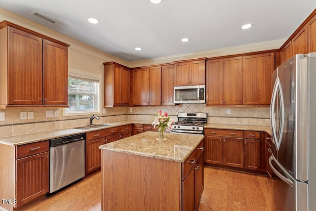 108 Holly Glen Ct, Holly Springs, NC 27540 - kitchen featuring stainless steel appliances, light wood-style flooring, ornamental molding, brown cabinets, and a center island