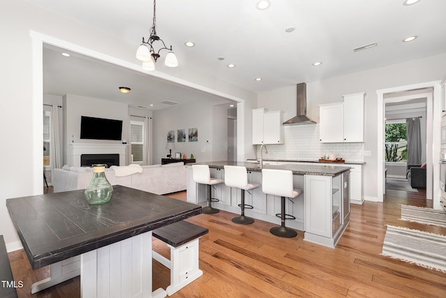 1502 Spring Overlook Ln, Hillsborough, NC 27278 - kitchen featuring wall chimney range hood, a breakfast bar, white cabinets, decorative backsplash, and light wood-type flooring