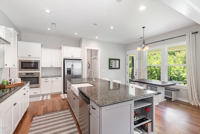1502 Spring Overlook Ln, Hillsborough, NC 27278 - kitchen with appliances with stainless steel finishes, a kitchen island with sink, backsplash, open shelves, and light wood finished floors