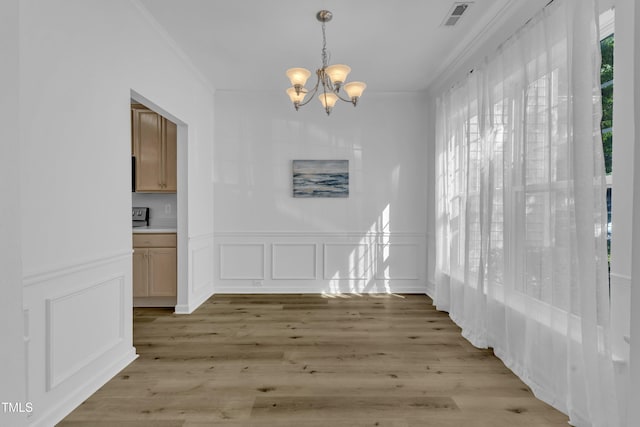11309 Shadow Elms Ln, Raleigh, NC 27614 - unfurnished dining area featuring a chandelier, crown molding, light wood finished floors, a decorative wall, and wainscoting