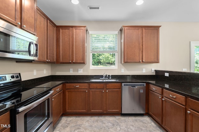 3417 Cardinal Lake Dr, Durham, NC 27704 - kitchen with appliances with stainless steel finishes, dark stone counters, brown cabinetry, stone finish floors, and recessed lighting