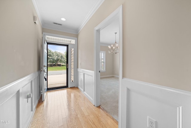 2022 Chandler Village Dr, Graham, NC 27253 - doorway featuring crown molding, a chandelier, a wainscoted wall, light wood-type flooring, and a decorative wall