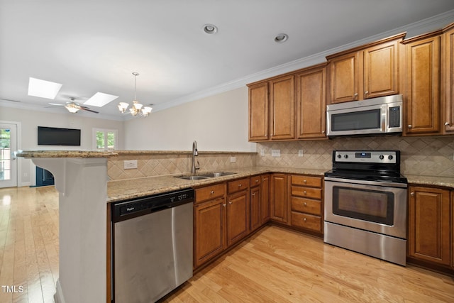 2022 Chandler Village Dr, Graham, NC 27253 - kitchen with appliances with stainless steel finishes, a skylight, a peninsula, brown cabinetry, and ornamental molding