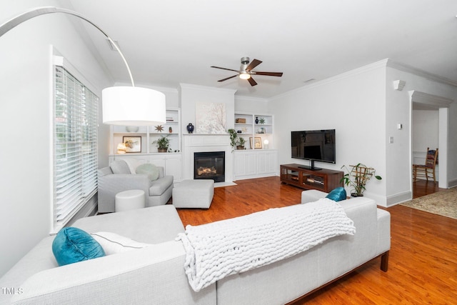 104 Homegate Cir, Apex, NC 27502 - living room with wood finished floors, a ceiling fan, crown molding, a fireplace with flush hearth, and built in shelves
