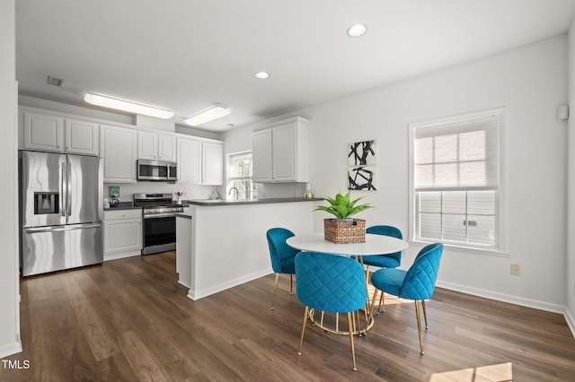 1308 Snyder St, Durham, NC 27713 - kitchen featuring appliances with stainless steel finishes, dark wood-style floors, a peninsula, recessed lighting, and white cabinetry