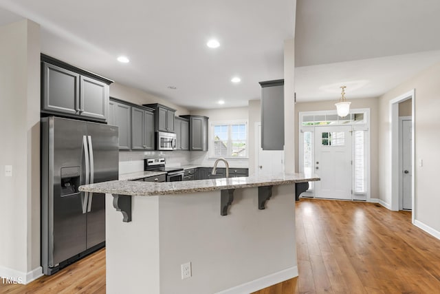 24 Windchime Ct, Clayton, NC 27527 - kitchen with stainless steel appliances, a kitchen bar, light stone countertops, a peninsula, and light wood-style floors