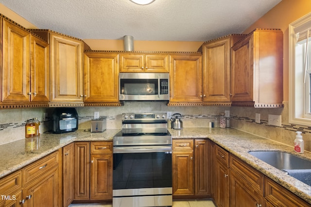 1401 Burchcrest Dr, Garner, NC 27529 - kitchen featuring appliances with stainless steel finishes, brown cabinetry, light stone countertops, and a textured ceiling
