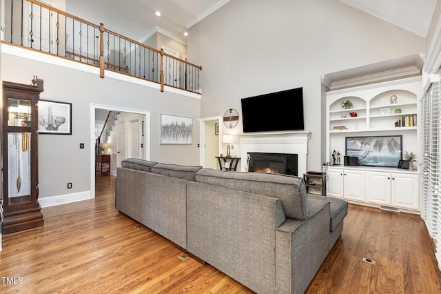 254 Charter Ct SE, Concord, NC 28025 - living room featuring a glass covered fireplace, wood finished floors, high vaulted ceiling, built in shelves, and stairway