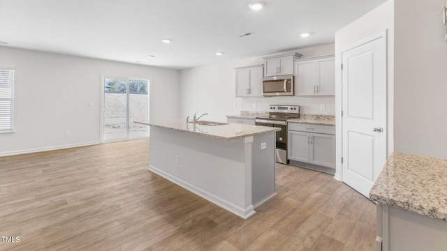 120 Leven Dr, Gibsonville, NC 27249 - kitchen with stainless steel appliances, light wood-type flooring, a kitchen island with sink, gray cabinets, and light stone countertops