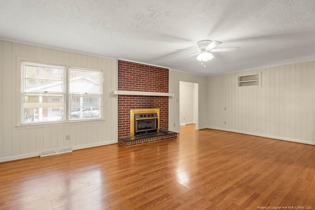 1905 N Rowland Ave N, Lumberton, NC 28358 - unfurnished living room featuring a ceiling fan, a textured ceiling, wood finished floors, a brick fireplace, and wooden walls