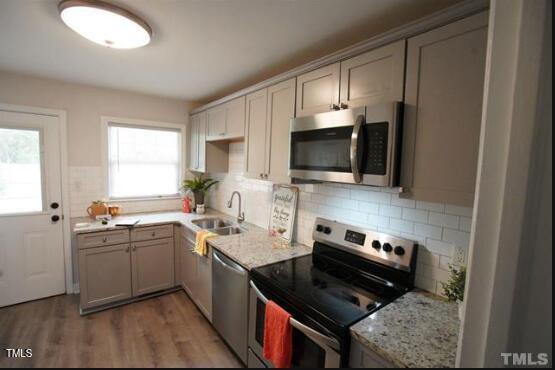 1206 Downing Rd, Raleigh, NC 27610 - kitchen featuring stainless steel appliances, backsplash, light wood-style flooring, gray cabinetry, and light stone counters