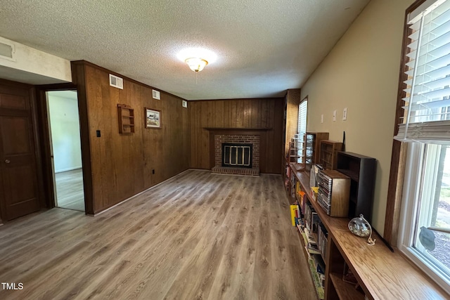609 Sloan Dr, Cary, NC 27511 - unfurnished living room with healthy amount of natural light, a textured ceiling, light wood-type flooring, a brick fireplace, and wood walls