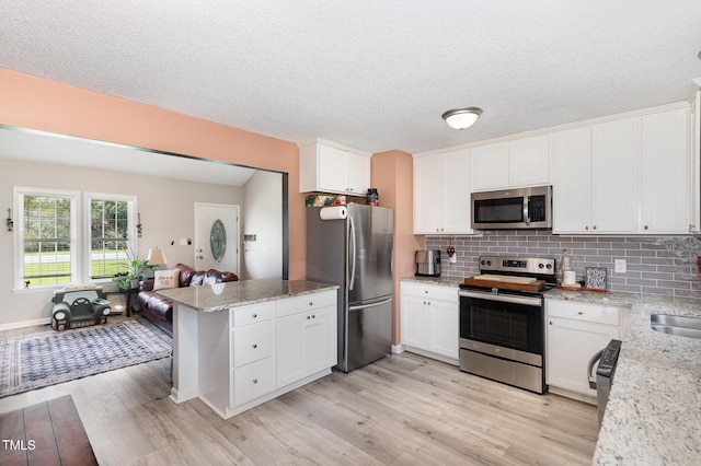 11 Sherman Rd, Fuquay Varina, NC 27526 - kitchen with stainless steel appliances, a peninsula, light wood-style flooring, white cabinets, and a textured ceiling