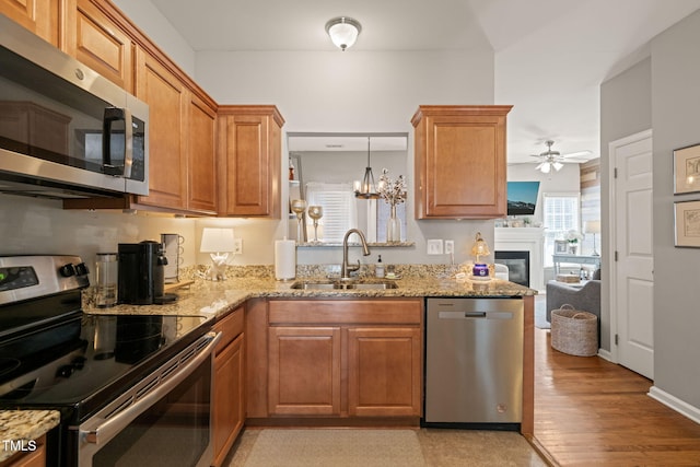 8221 Hempshire Pl Unit 101, Raleigh, NC 27613 - kitchen with appliances with stainless steel finishes, a ceiling fan, light stone counters, a glass covered fireplace, and brown cabinetry