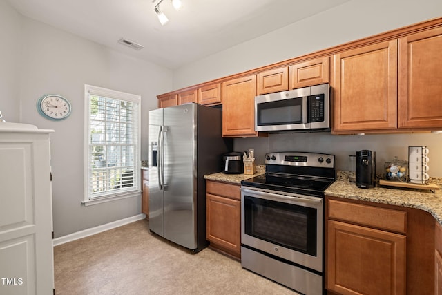 8221 Hempshire Pl Unit 101, Raleigh, NC 27613 - kitchen featuring stainless steel appliances, light colored carpet, light stone counters, and brown cabinetry