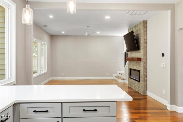 7414 Brandon Allen Ave, Raleigh, NC 27613 - kitchen with wood finished floors, ceiling fan, a tiled fireplace, light countertops, and open floor plan