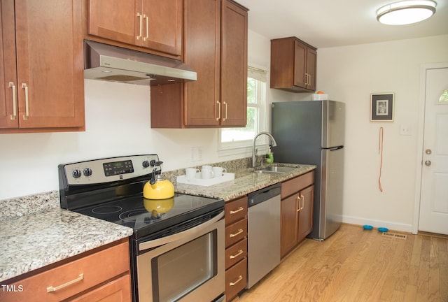 4028 Chaucer Dr, Durham, NC 27705 - kitchen featuring appliances with stainless steel finishes, under cabinet range hood, light wood-type flooring, light stone countertops, and brown cabinetry