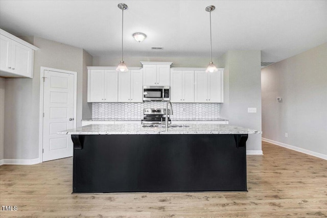 106 Fynloch Chase Dr, Fremont, NC 27830 - kitchen featuring appliances with stainless steel finishes, white cabinets, light wood-type flooring, backsplash, and a center island with sink