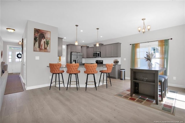 208 Walker Downs Cir, Fayetteville, NC 28305 - kitchen with stainless steel appliances, gray cabinetry, a kitchen breakfast bar, light wood-type flooring, and a chandelier