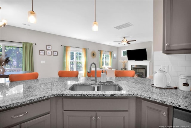 208 Walker Downs Cir, Fayetteville, NC 28305 - kitchen with gray cabinets, backsplash, ceiling fan, a fireplace, and light stone counters