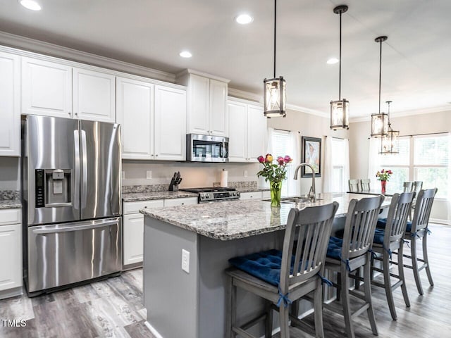 3441 Jordan Shires Dr, New Hill, NC 27562 - kitchen featuring appliances with stainless steel finishes, ornamental molding, light wood-style flooring, white cabinetry, and a kitchen island with sink