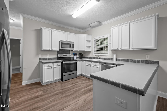 116 Justice St, Chapel Hill, NC 27516 - kitchen with appliances with stainless steel finishes, a peninsula, wood finished floors, white cabinetry, and a textured ceiling