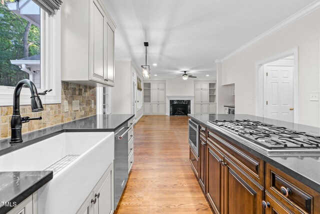 105 Bathgate Ln, Cary, NC 27513 - kitchen featuring appliances with stainless steel finishes, a ceiling fan, ornamental molding, a fireplace, and light wood-type flooring