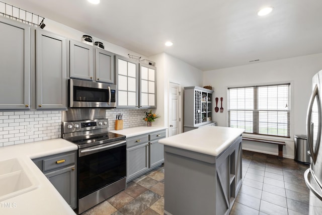 8205 Rolling Glenn Dr, Raleigh, NC 27616 - kitchen featuring stainless steel appliances, gray cabinets, decorative backsplash, light countertops, and a kitchen island