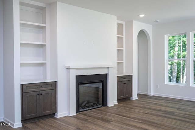 6069 Jones Cir, Sanford, NC 27332 - unfurnished living room featuring built in shelves, dark wood finished floors, a glass covered fireplace, and arched walkways