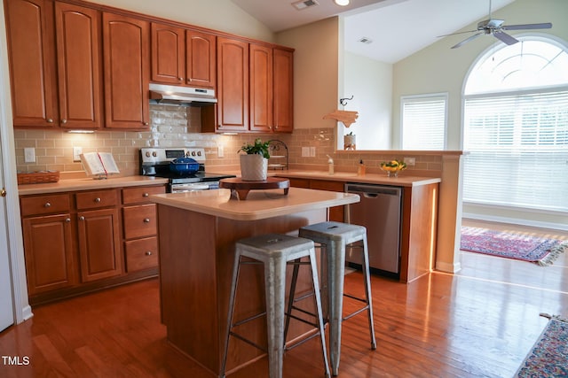 3423 Van Hessen Dr, Raleigh, NC 27614 - kitchen with appliances with stainless steel finishes, under cabinet range hood, lofted ceiling, a peninsula, and wood finished floors