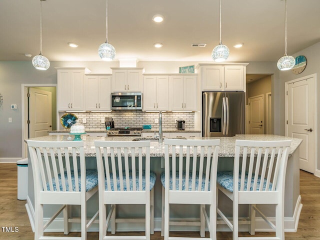 67 Blue Spruce Cir, Clayton, NC 27527 - kitchen featuring stainless steel appliances, a spacious island, decorative backsplash, light wood finished floors, and white cabinets