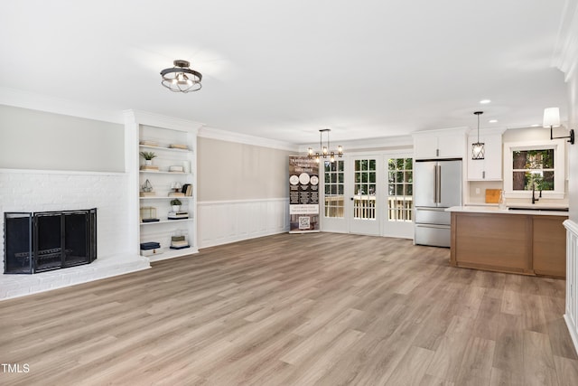 1609 Falls Ct, Raleigh, NC 27615 - unfurnished living room with ornamental molding, light wood-type flooring, a chandelier, a wainscoted wall, and a brick fireplace