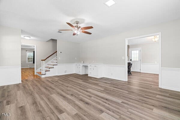 509 S Mckay Ave, Dunn, NC 28334 - unfurnished living room featuring ceiling fan, stairway, a wainscoted wall, and wood finished floors