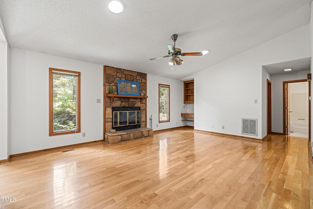 601 Wofford Rd, Durham, NC 27707 - unfurnished living room featuring a textured ceiling, vaulted ceiling, light wood-style flooring, a ceiling fan, and a stone fireplace