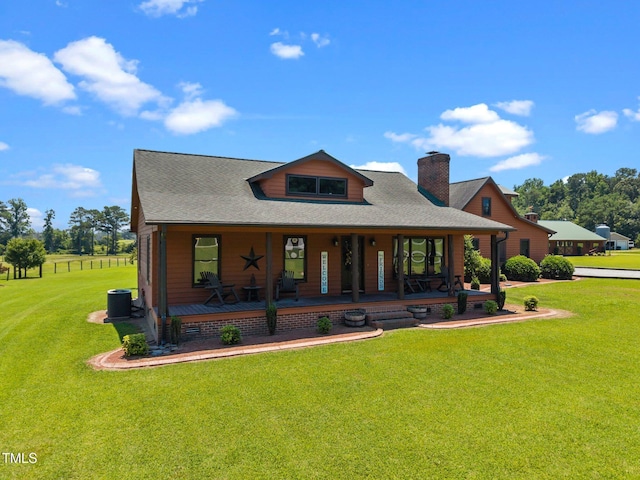 view of front facade featuring a chimney, covered porch, a front yard, and roof with shingles